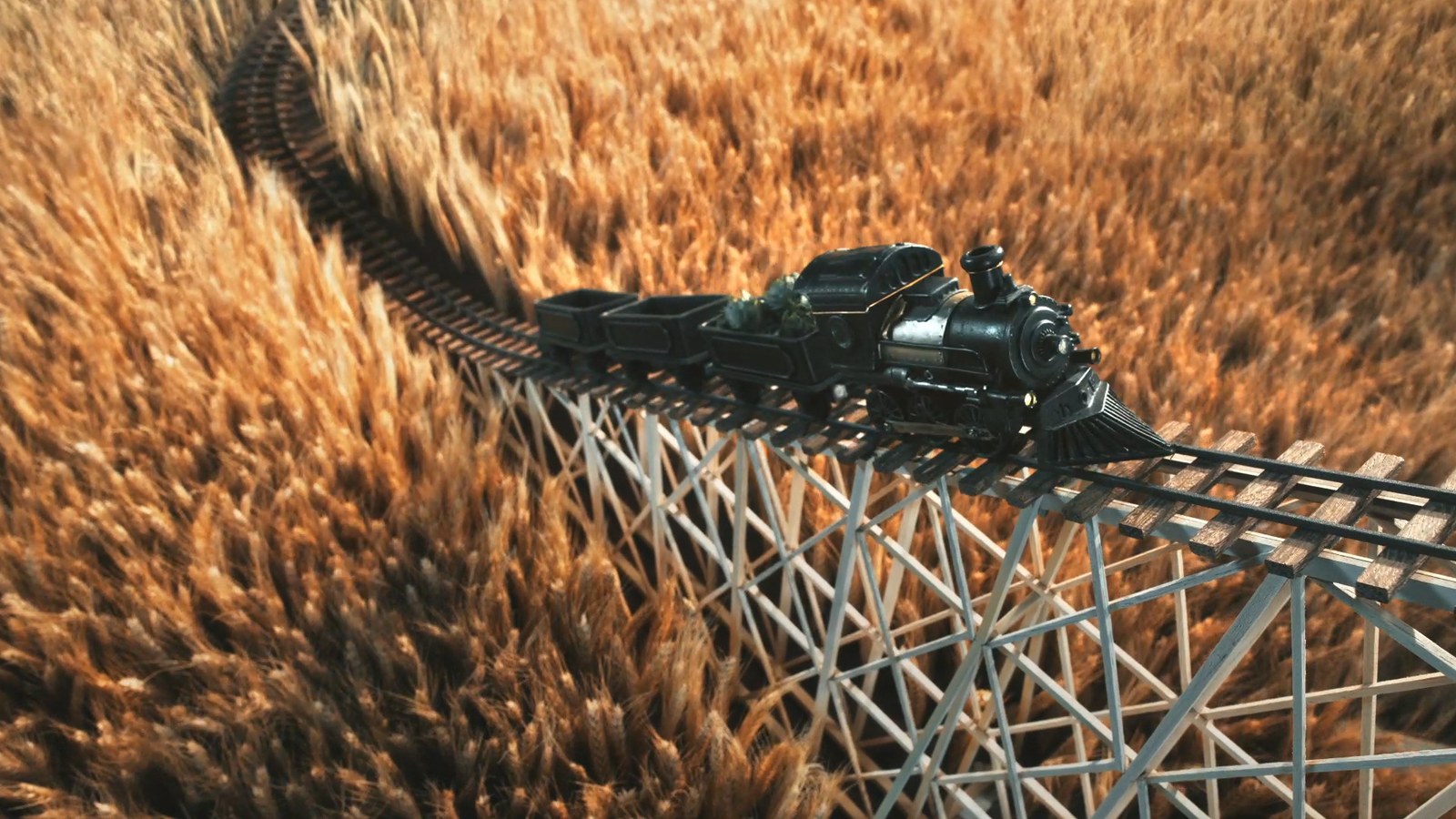 The model train crossing a wooden trestle through a field of wheat