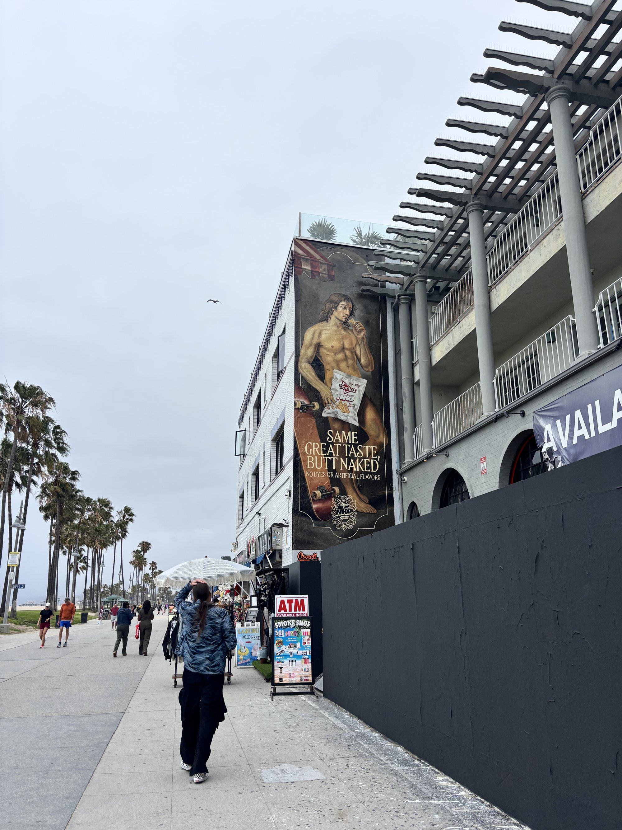 A person walking the Venice boardwalk with the mural rising behind