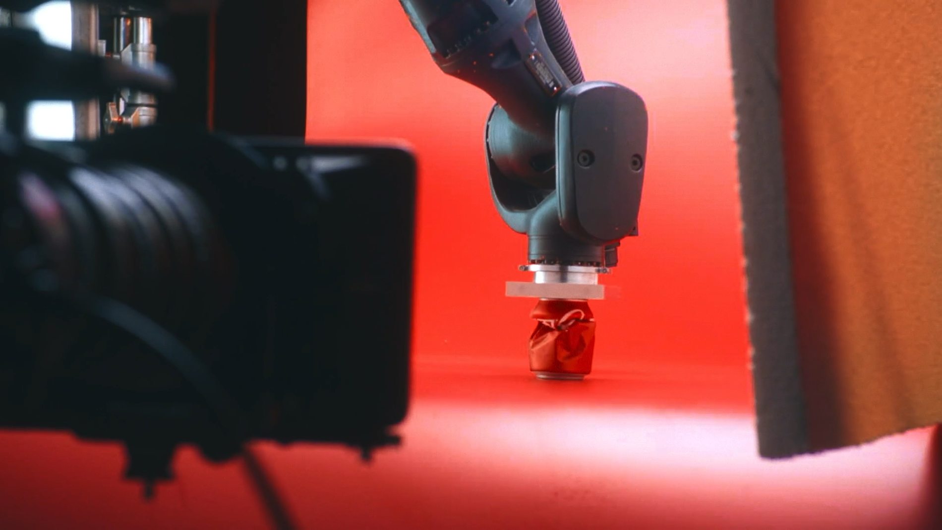 A robot arm pressing a Coca-Cola can on the red-lit set
