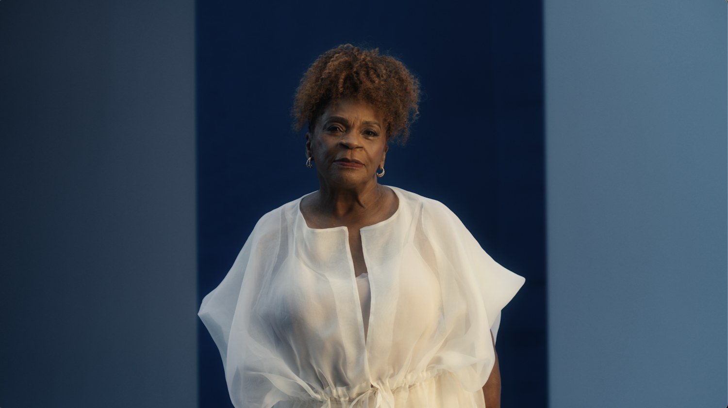 An older actress in white against the blue set